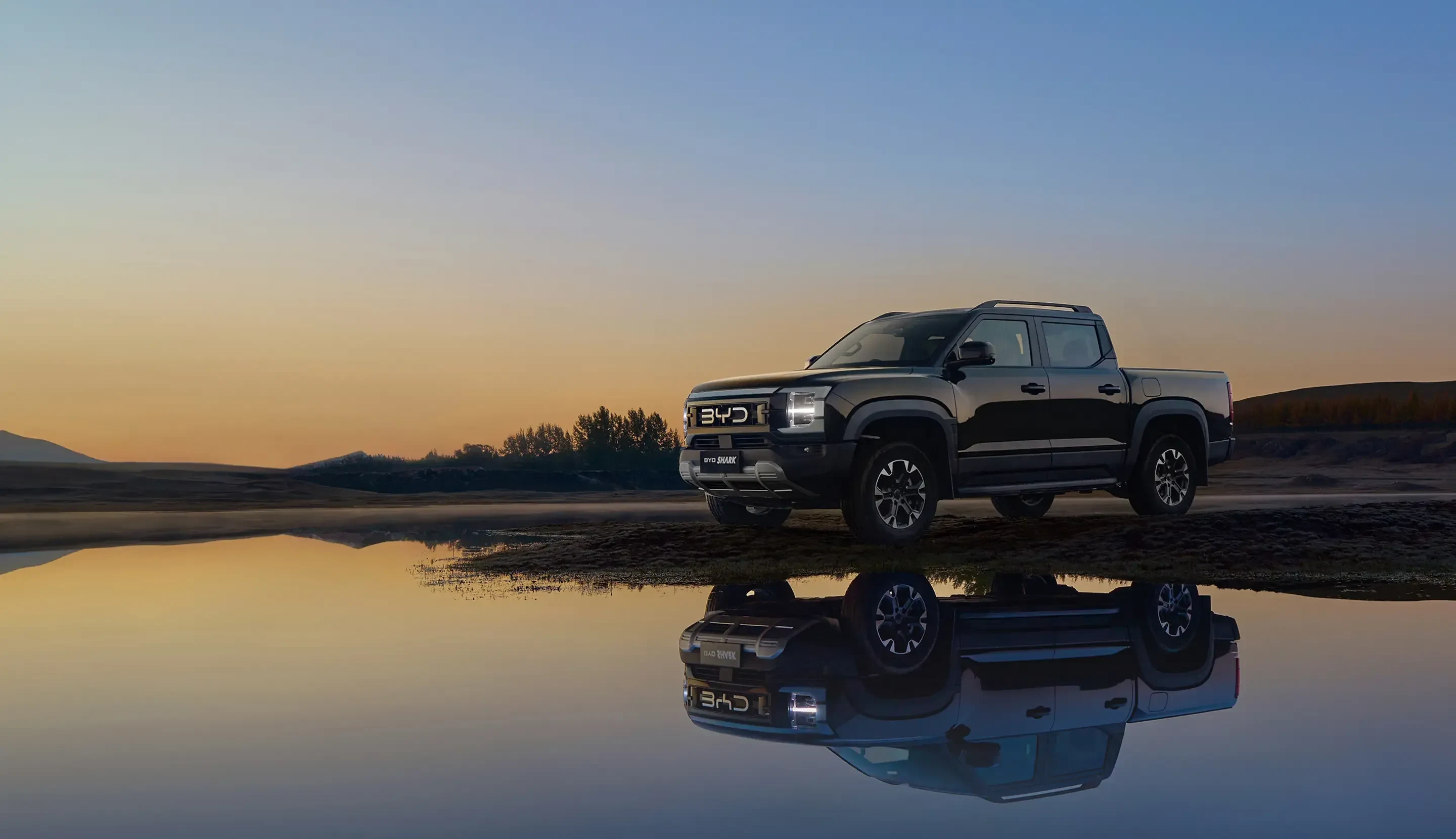 BYD Shark ao pôr do sol, refletida na água em uma paisagem aberta